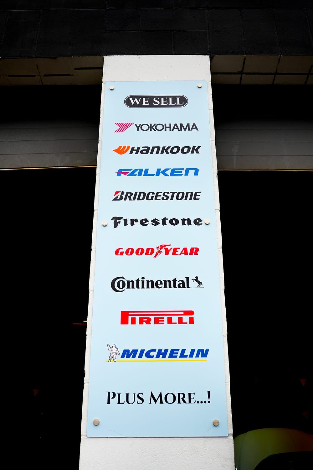 Shop sign listing the tire brands sold: Yokohama, Hankook, Falken, Bridgestone, Firestone, Goodyear, Continental, Pirelli, Michelin and more
